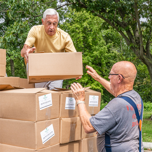 Two older men volunteering at Families Matter Food Pantry by unloading boxes of food from a truck